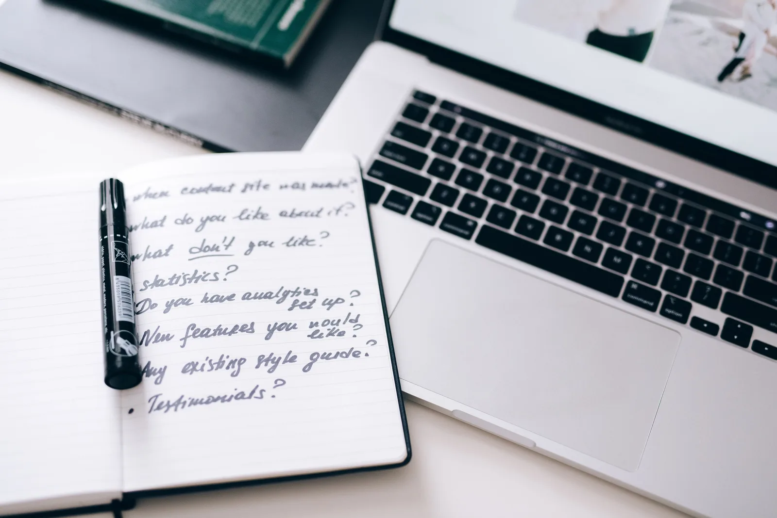 A notebook with handwritten notes next to a laptop on a workspace desk.