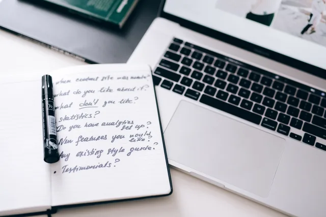 A notebook with handwritten notes next to a laptop on a workspace desk. Choosing B2B influencer marketing survey tools without the guesswork