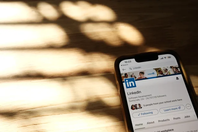 Close-up of a smartphone showing a LinkedIn profile page on a wooden table with shadows. B2B influencer marketing vs employee advocacy in the UK: a decision table with the legal duties on each route